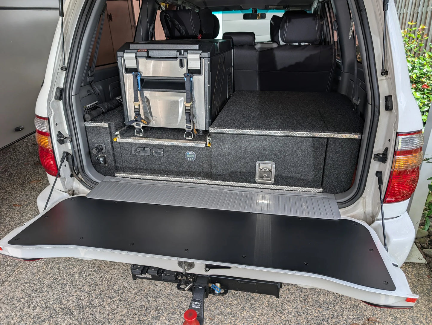 Black tailgate chopping board food preparation surface installed on the open lower tailgate of a Toyota LandCruiser 100 or 105 Series 4WD vehicle