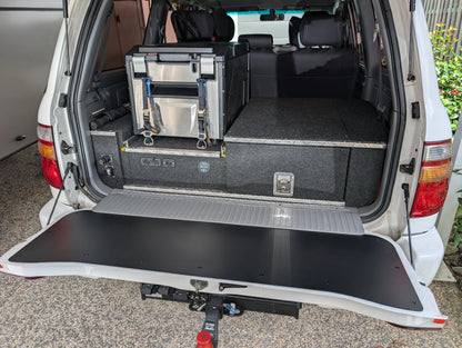 Black tailgate chopping board food preparation surface installed on the open lower tailgate of a Toyota LandCruiser 100 or 105 Series 4WD vehicle