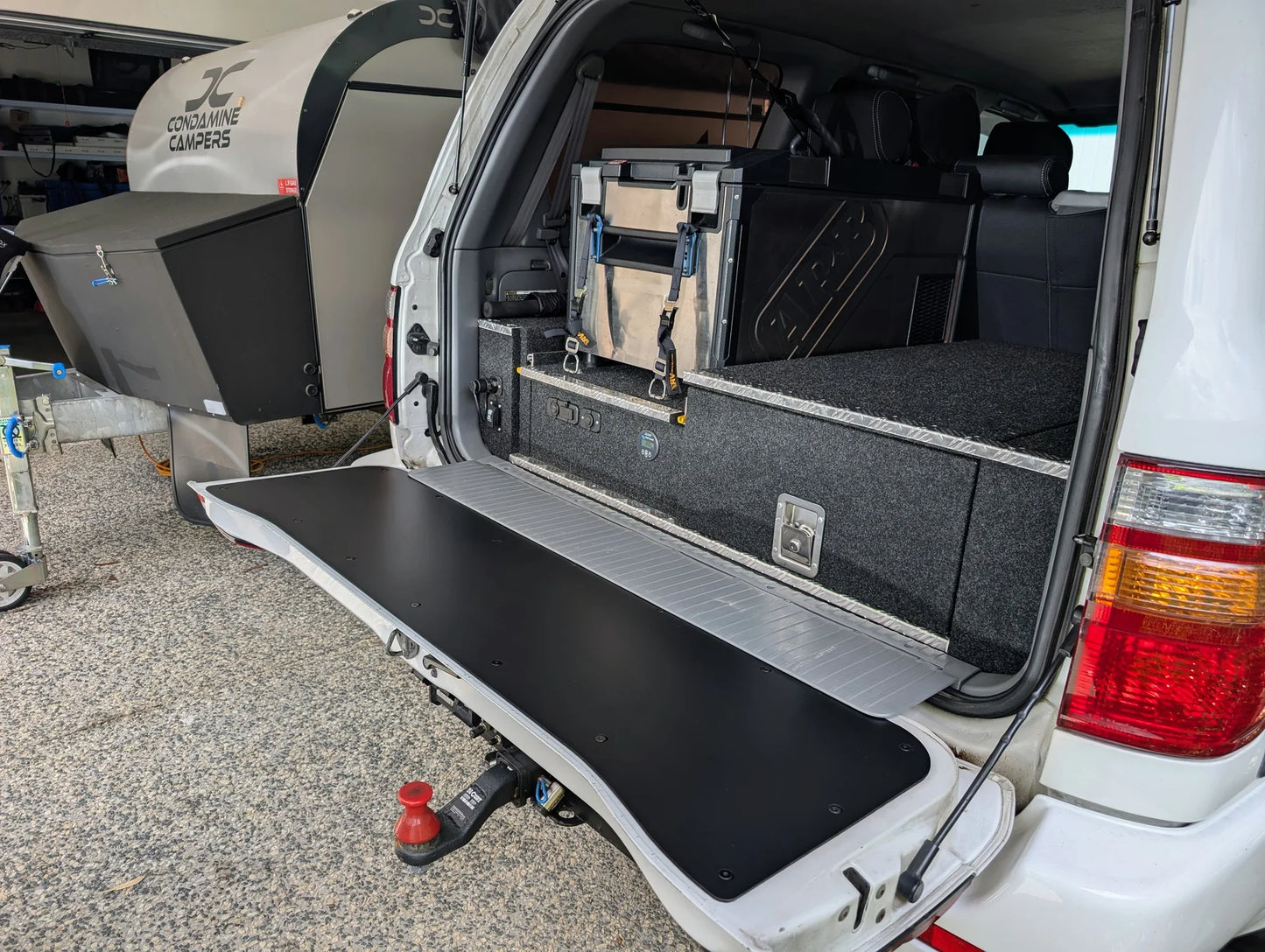 Black tailgate chopping board food preparation surface installed on the open lower tailgate of a Toyota LandCruiser 100 or 105 Series 4WD vehicle.