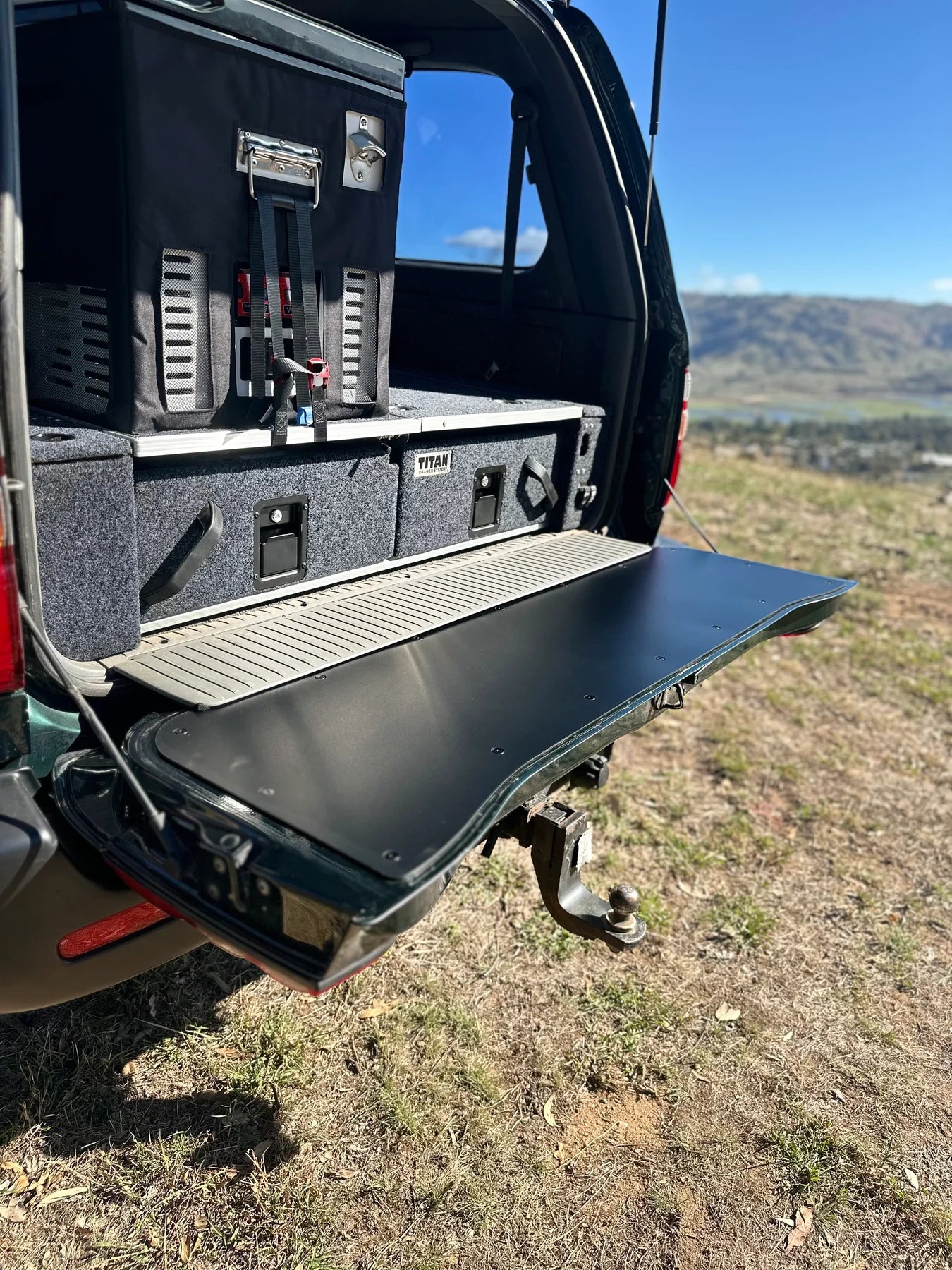 Black tailgate chopping board food preparation surface installed on the open lower tailgate of a Toyota LandCruiser 100 or 105 Series 4WD vehicle.