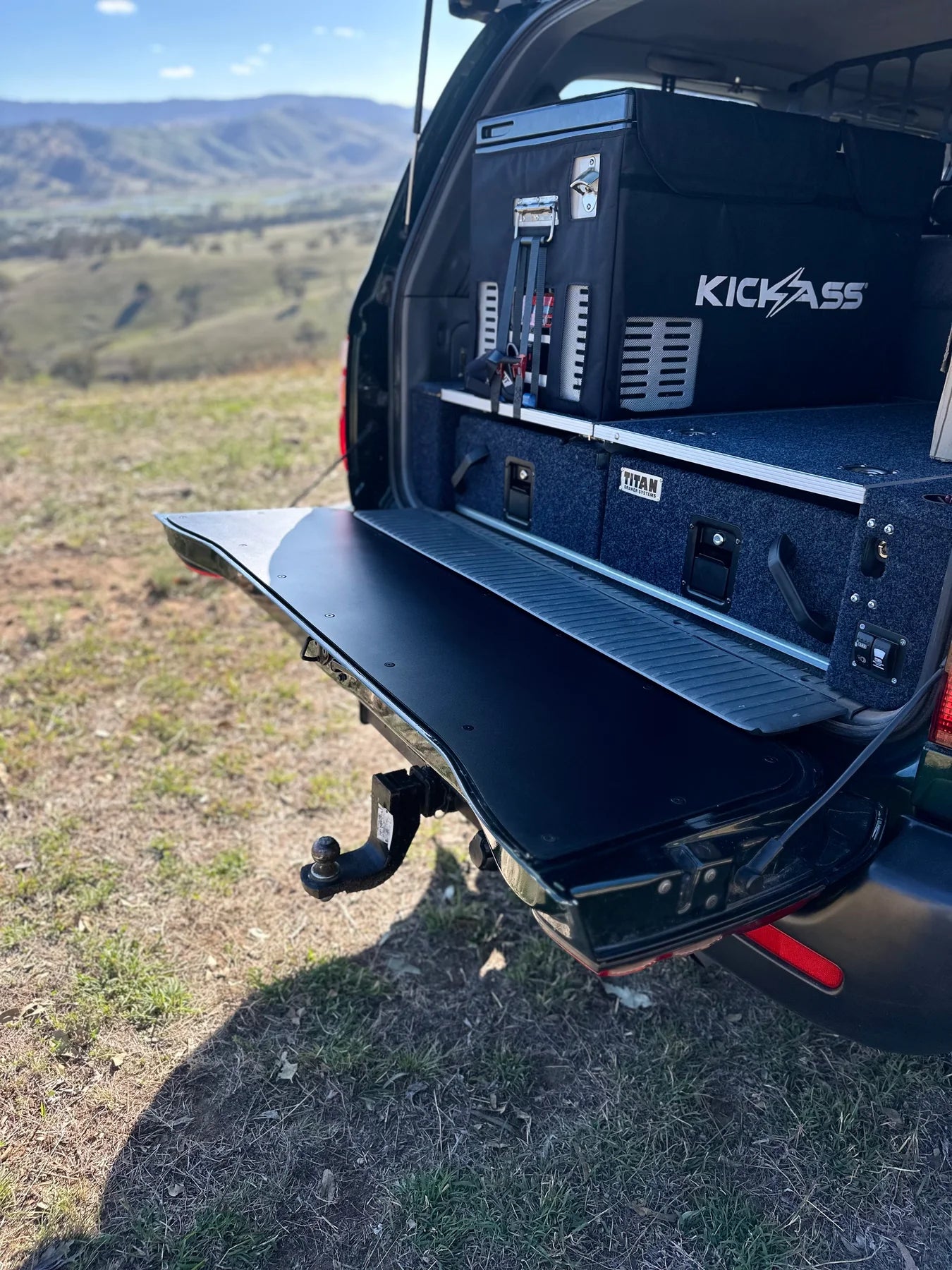 Black tailgate chopping board food preparation surface installed on the open lower tailgate of a Toyota LandCruiser 100 or 105 Series 4WD vehicle.